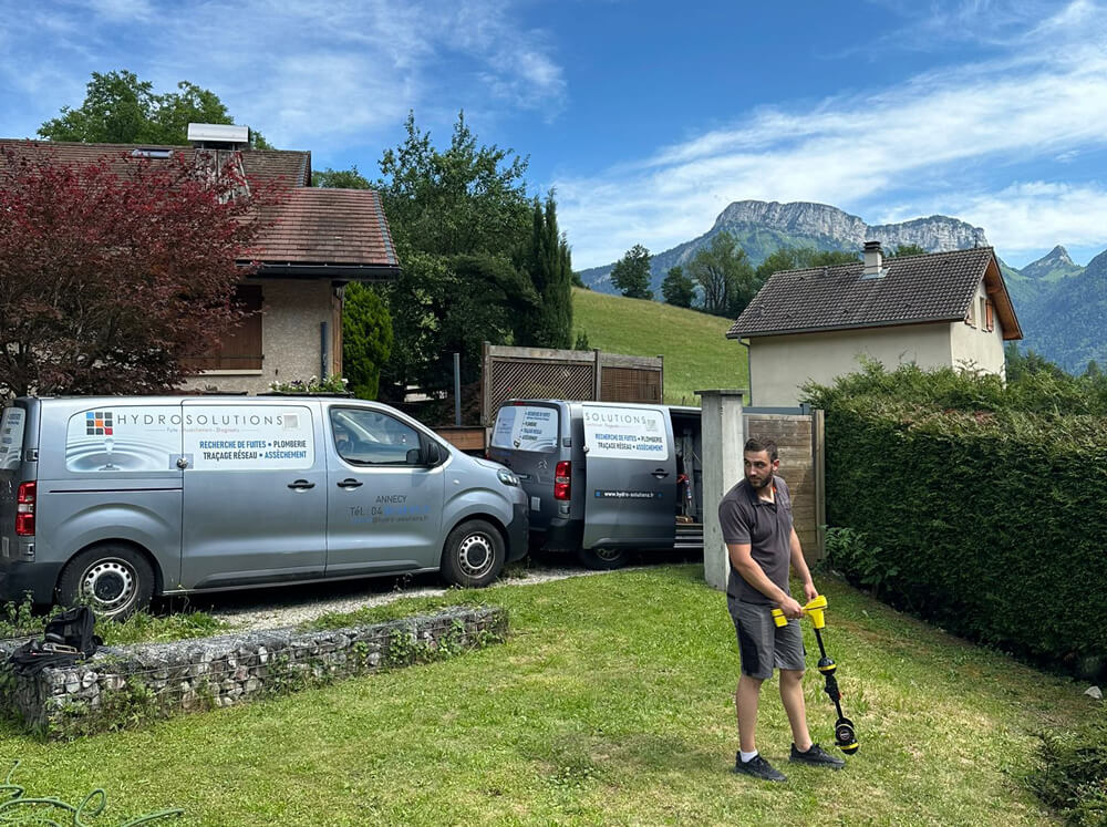 Technicien d'Hydrosolutions cherchant une fuite et camions de l'entreprise garés devant un lotissement